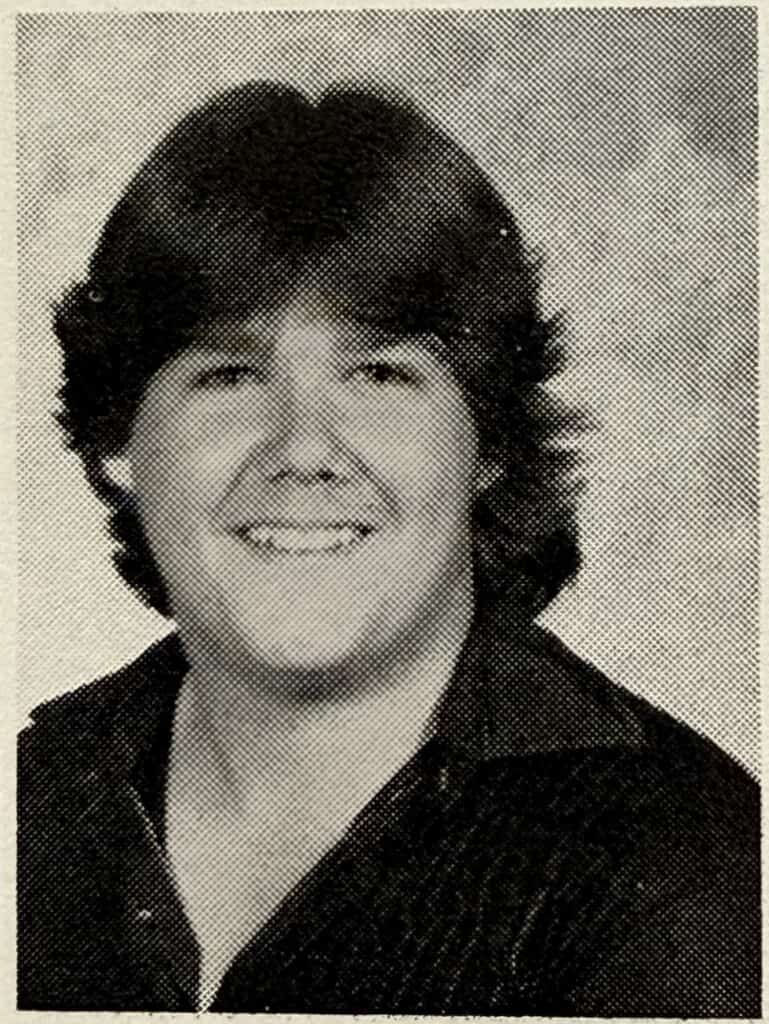 A black-and-white yearbook photo of a young person with medium-length, feathered hair, smiling and wearing a dark collared shirt—capturing the sincerity often seen in a christian testimony, posed in front of a plain backdrop.